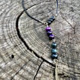 Collier unisex KIM Collier unisex KIM repositionnable Collier Kim, ajustable. Collier pour homme, collier pour femme. Bijou homme Kim, bijou femme Kim, avec lanière en cuir noir, oeil de faucon et oeil de tigre violet et une breloque de plume de couleur bronze. Un bijou de cou unisex KIM qui peut être commandé pour les deux genres et partagé ou commandé en d’autres couleurs et on peur les échanger et superposer pour le porter.
