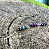 Collier unisex KIM Collier unisex KIM repositionnable Collier Kim, ajustable. Collier pour homme, collier pour femme. Bijou homme Kim, bijou femme Kim, avec lanière en cuir noir, oeil de faucon et oeil de tigre violet et une breloque de plume de couleur bronze. Un bijou de cou unisex KIM qui peut être commandé pour les deux genres et partagé ou commandé en d’autres couleurs et on peur les échanger et superposer pour le porter.