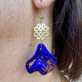 Boucles d’oreilles Flavie Découvrez les boucles d’oreilles “Flavie”, des bijoux fantaisie uniques en leur genre. Déclinées en plusieurs couleurs tendance  – blanc mat, rose métallisé, vert foncé métallisé, bleu royal mat, rouge métallisé et or – elles offrent une touche de raffinement avec leurs projections de couleur or, appliquées à la main pour une finition singulière sur chaque paire. Le design inclut un élément doré élégant et une pétale suspendue de couleur tachetée or, rendant ces boucles d’oreilles idéales pour compléter vos tenues au quotidien ou pour des occasions spéciales. Créées par l’artiste Jana Kuzmi, elles représentent un accessoire original et de qualité qui saura se démarquer dans votre collection de bijoux.