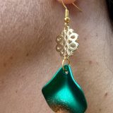 Boucles d’oreilles Flavie Découvrez les boucles d’oreilles “Flavie”, des bijoux fantaisie uniques en leur genre. Déclinées en plusieurs couleurs tendance  – blanc mat, rose métallisé, vert foncé métallisé, bleu royal mat, rouge métallisé et or – elles offrent une touche de raffinement avec leurs projections de couleur or, appliquées à la main pour une finition singulière sur chaque paire. Le design inclut un élément doré élégant et une pétale suspendue de couleur tachetée or, rendant ces boucles d’oreilles idéales pour compléter vos tenues au quotidien ou pour des occasions spéciales. Créées par l’artiste Jana Kuzmi, elles représentent un accessoire original et de qualité qui saura se démarquer dans votre collection de bijoux.
