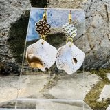 Boucles d’oreilles Flavie Découvrez les boucles d’oreilles “Flavie”, des bijoux fantaisie uniques en leur genre. Déclinées en plusieurs couleurs tendance  – blanc mat, rose métallisé, vert foncé métallisé, bleu royal mat, rouge métallisé et or – elles offrent une touche de raffinement avec leurs projections de couleur or, appliquées à la main pour une finition singulière sur chaque paire. Le design inclut un élément doré élégant et une pétale suspendue de couleur tachetée or, rendant ces boucles d’oreilles idéales pour compléter vos tenues au quotidien ou pour des occasions spéciales. Créées par l’artiste Jana Kuzmi, elles représentent un accessoire original et de qualité qui saura se démarquer dans votre collection de bijoux.