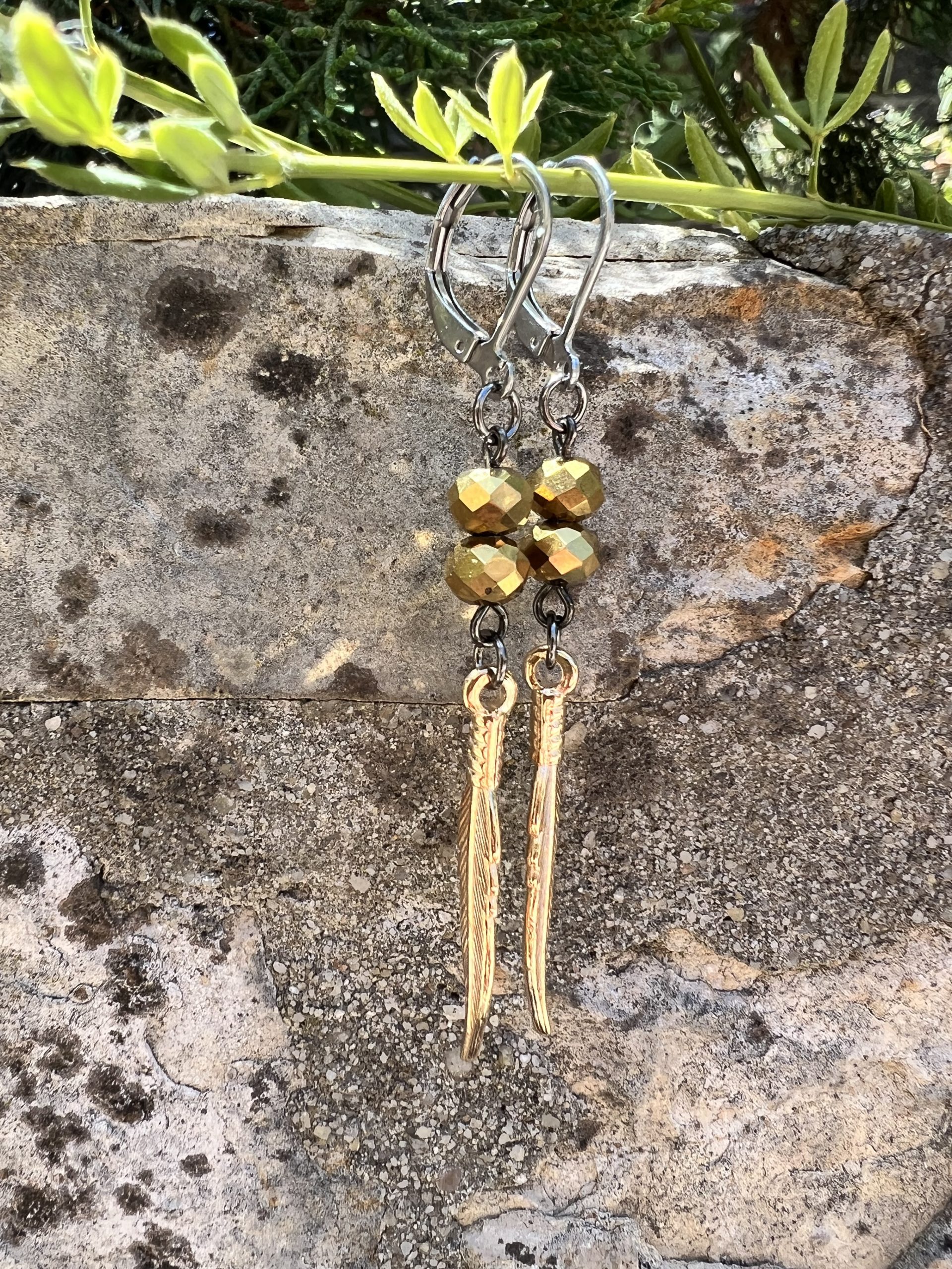 Boucles d'oreilles Plume or Les magnifiques boucles d'oreilles pendantes en style bohème, conçues à la main par l'artiste Jana Kuzmi, peintre et créatrice de bijoux de fantaisie. Ornées d'une plume dure de couleur or, elles apportent une touche d'élégance et de légèreté à votre look. Les attaches en acier inoxydable gris foncé garantissent confort et durabilité, tandis que les perles dorées ajoutent une note sophistiquée. Boucles d'oreilles Plume or Parfaites pour une allure bohème chic, ces bijoux uniques sont idéaux pour sublimer vos tenues avec style et originalité. Offrez-vous un accessoire artisanal de qualité, alliant créativité et élégance, signé Jana Kuzmi.