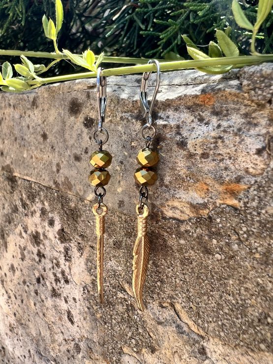 Boucles d'oreilles Plume or Les magnifiques boucles d'oreilles pendantes en style bohème, conçues à la main par l'artiste Jana Kuzmi, peintre et créatrice de bijoux de fantaisie. Ornées d'une plume dure de couleur or, elles apportent une touche d'élégance et de légèreté à votre look. Les attaches en acier inoxydable gris foncé garantissent confort et durabilité, tandis que les perles dorées ajoutent une note sophistiquée. Boucles d'oreilles Plume or Parfaites pour une allure bohème chic, ces bijoux uniques sont idéaux pour sublimer vos tenues avec style et originalité. Offrez-vous un accessoire artisanal de qualité, alliant créativité et élégance, signé Jana Kuzmi.