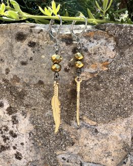 Boucles d'oreilles Plume or Les magnifiques boucles d'oreilles pendantes en style bohème, conçues à la main par l'artiste Jana Kuzmi, peintre et créatrice de bijoux de fantaisie. Ornées d'une plume dure de couleur or, elles apportent une touche d'élégance et de légèreté à votre look. Les attaches en acier inoxydable gris foncé garantissent confort et durabilité, tandis que les perles dorées ajoutent une note sophistiquée. Boucles d'oreilles Plume or Parfaites pour une allure bohème chic, ces bijoux uniques sont idéaux pour sublimer vos tenues avec style et originalité. Offrez-vous un accessoire artisanal de qualité, alliant créativité et élégance, signé Jana Kuzmi.