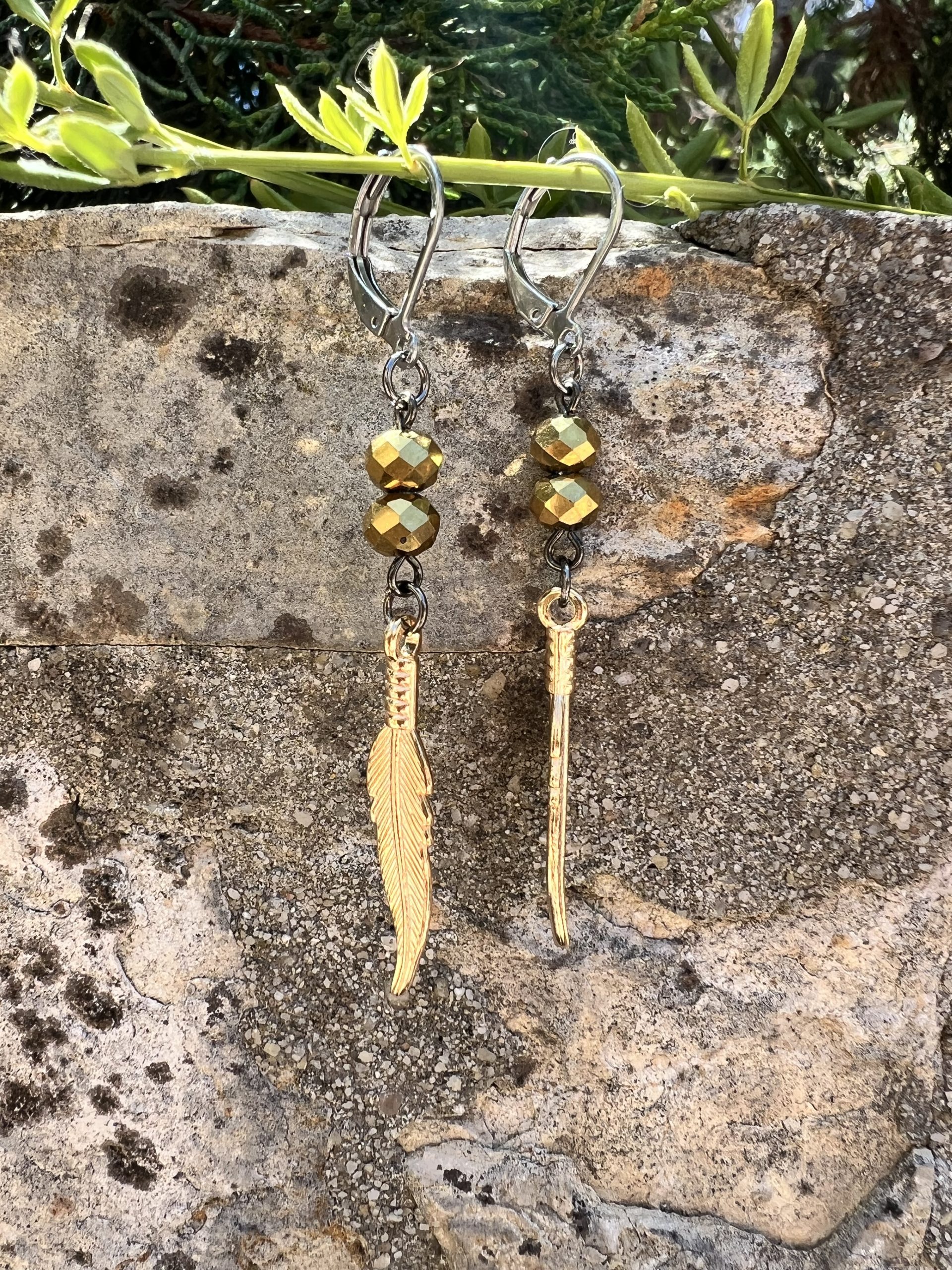 Boucles d'oreilles Plume or Les magnifiques boucles d'oreilles pendantes en style bohème, conçues à la main par l'artiste Jana Kuzmi, peintre et créatrice de bijoux de fantaisie. Ornées d'une plume dure de couleur or, elles apportent une touche d'élégance et de légèreté à votre look. Les attaches en acier inoxydable gris foncé garantissent confort et durabilité, tandis que les perles dorées ajoutent une note sophistiquée. Boucles d'oreilles Plume or Parfaites pour une allure bohème chic, ces bijoux uniques sont idéaux pour sublimer vos tenues avec style et originalité. Offrez-vous un accessoire artisanal de qualité, alliant créativité et élégance, signé Jana Kuzmi.