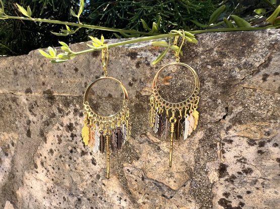 Boucles d'oreilles - Attrape rêve Boucles d'oreilles artisanales avec plumes colorées/teintes dorées et argentées – Attrape-rêves fait main par Jana Kuzmi | Boucle Bel Air Découvrez nos magnifiques boucles d'oreilles artisanales, conçues avec soin par l'artiste Jana Kuzmi sous la marque Boucle Bel Air. Chaque paire met en valeur des plumes dures de différentes couleurs, attachées à un cercle qui forme un attrape-rêves unique et élégant. Parfaites pour ajouter une touche bohème et colorée à votre style, ces boucles d'oreilles faites main sont idéales pour les amoureux de l'artisanat et de la mode éthique. Boucles d'oreilles - Attrape rêve Offrez-vous un accessoire original, léger et plein de charme, qui reflète la créativité et le savoir-faire de Jana Kuzmi. Caractéristiques principales : Création artisanale par Jana Kuzmi Design attrape-rêves avec plumes colorées Boucles d'oreilles faites main Matériaux de qualité, plumes dures résistantes Idéal pour un style bohème, ethnique ou tendance Ajoutez une touche d'originalité à votre collection avec ces, Boucles d'oreilles - Attrape rêve, uniques, parfaites pour toutes les occasions. 