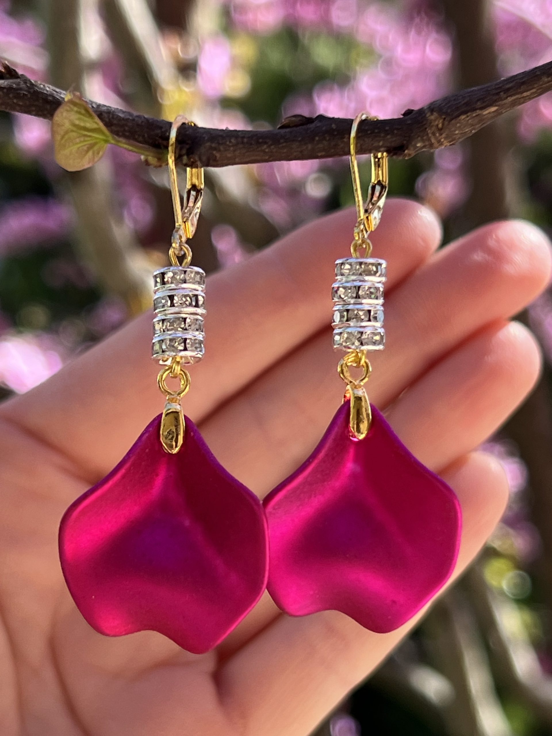 Boucles d’oreilles roses fuchsia avec brillants - Pinky — Création de Jana KUZMI Boucles d’oreilles pendantes fuchsia et dorées, ornées de zircons transparents — création originale réalisée à la main par Jana KUZMI. Laissez-vous séduire par « Pinky », une paire de boucles d’oreilles aussi lumineuses qu’audacieuses, imaginées et réalisées à la main par l’artiste Jana KUZMI.  Leurs pétales rose fuchsia métallisé captent délicatement la lumière et apportent une touche de couleur vibrante à votre tenue. Au-dessus, les entretoises finement ornées de zircons transparents ajoutent une subtile note de lumière et d’élégance. Les boucles sont montées sur des attaches sécurisées en acier inoxydable doré, pensées pour assurer un maintien confortable tout en sublimant la finesse de la création. Une création rose qui ne passe pas inaperçue Avec leur silhouette pendante et leur association de rose fuchsia, d’or et de brillants transparents, les boucles « Pinky » sont idéales pour celles qui aiment les bijoux originaux, féminins et lumineux. Elles peuvent accompagner aussi bien une tenue élégante qu'un look plus contemporain et apporter instantanément une touche de personnalité. Chaque paire est réalisée à la main par Jana KUZMI : vous choisissez ainsi une création artistique qui possède son propre caractère, loin des bijoux standardisés de la grande distribution. « Pinky » — parce qu’un bijou peut être bien plus qu’un accessoire : une petite œuvre à porter.  Caractéristiques : Boucles d’oreilles pendantes Création originale réalisée à la main Pétales rose fuchsia métallisé Entretoises ornées de zircons transparents Attaches sécurisées Acier inoxydable finition dorée Création signée Jana KUZMI Bijou original et féminin, idéal pour offrir ou se faire plaisir